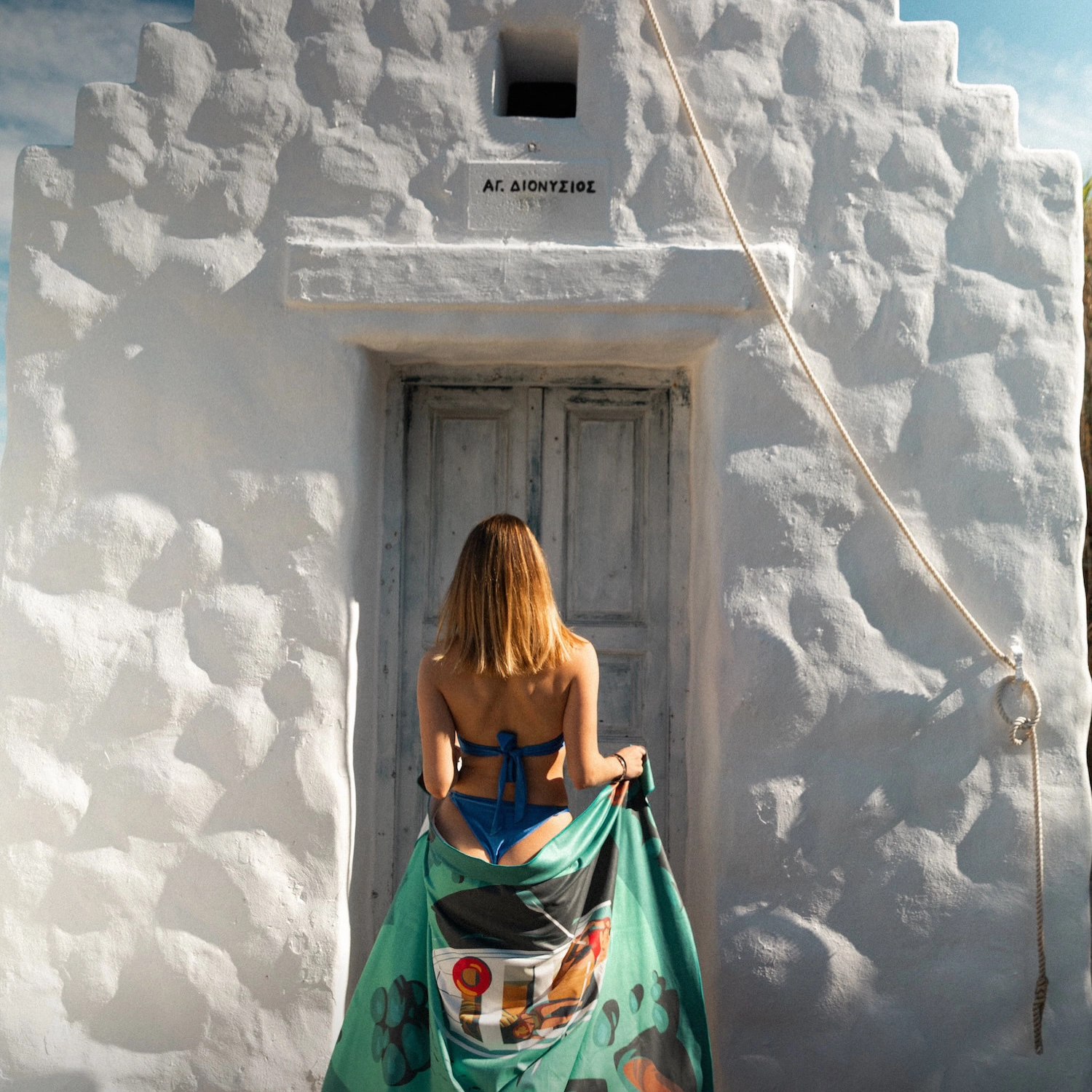 Woman wearing a One Zipper microfibre beach towel in a Greek island setting